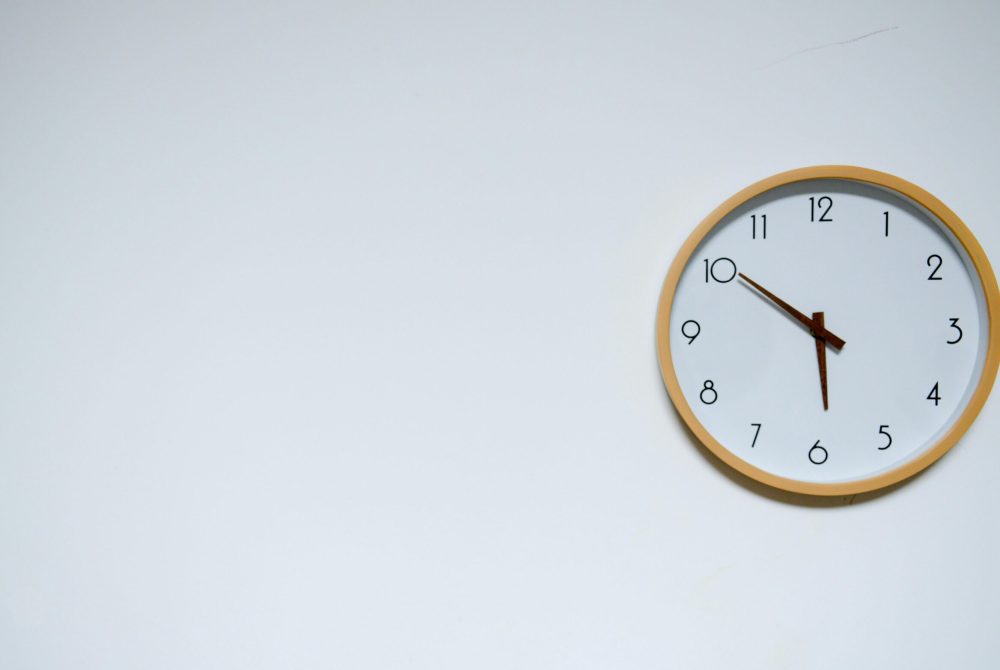 Simple wall clock with wooden frame against a white background, showing the time 10:10.